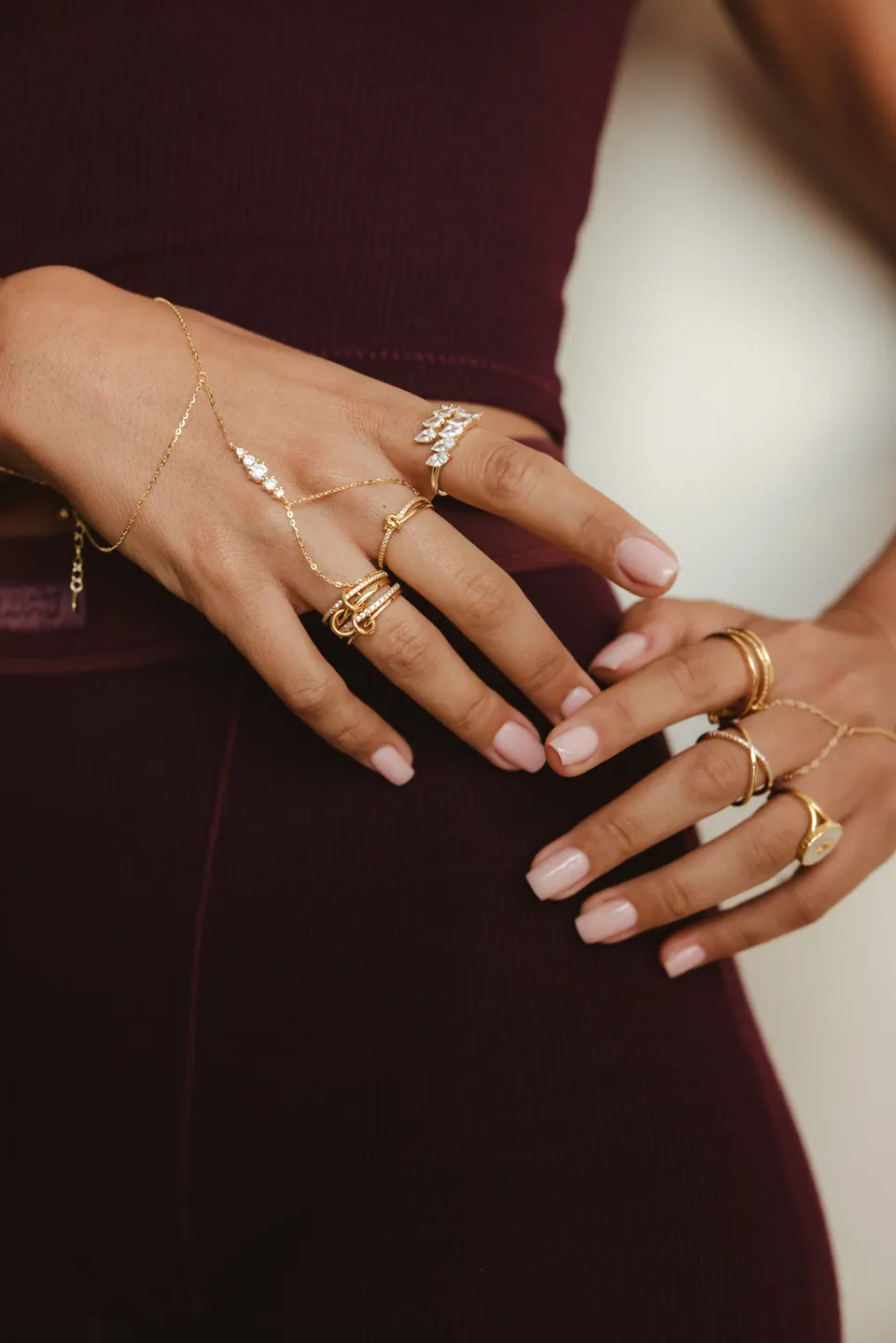 Close view of two hands on a burgundy outfit, wearing rings and hand chains.