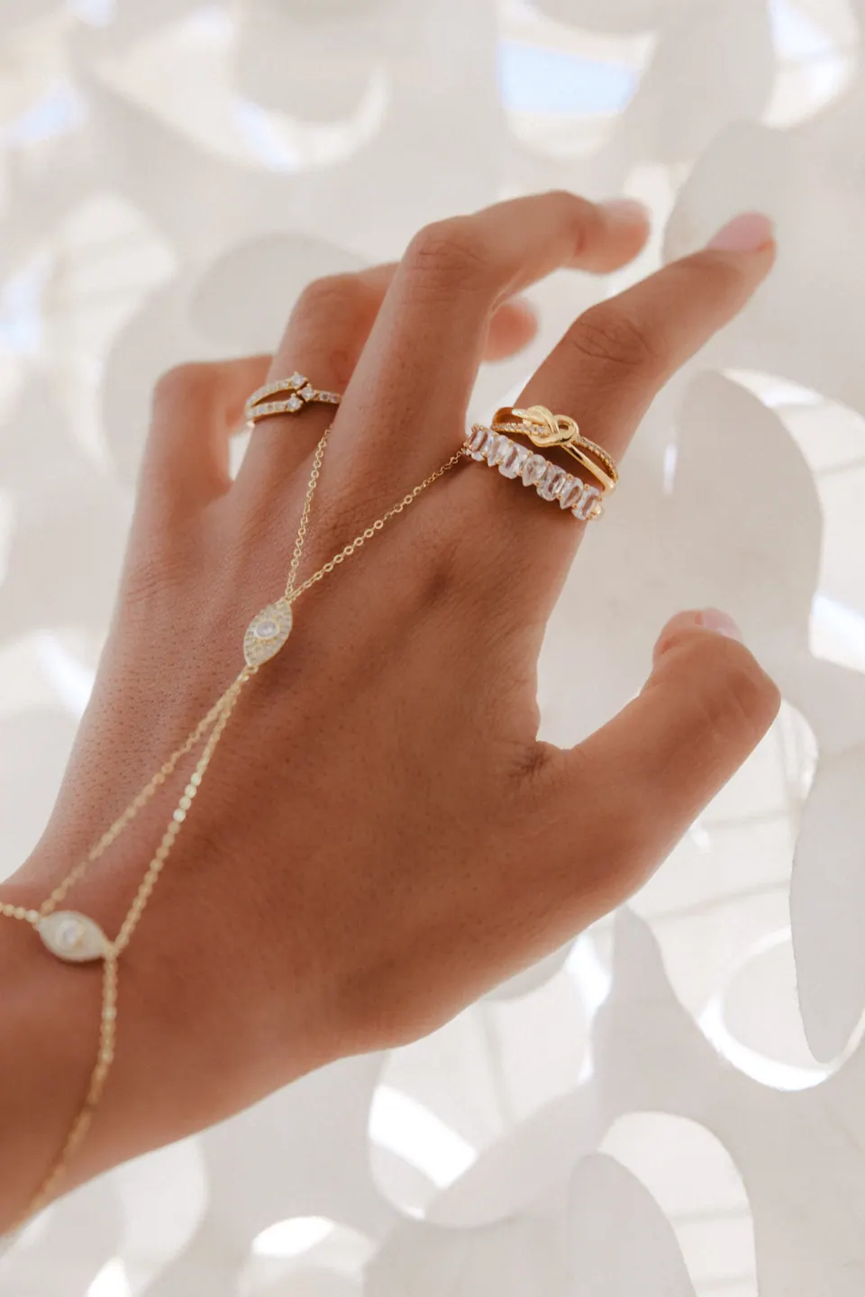 Close-up of a hand wearing rings and a hand chain against a backdrop of white paper petals.