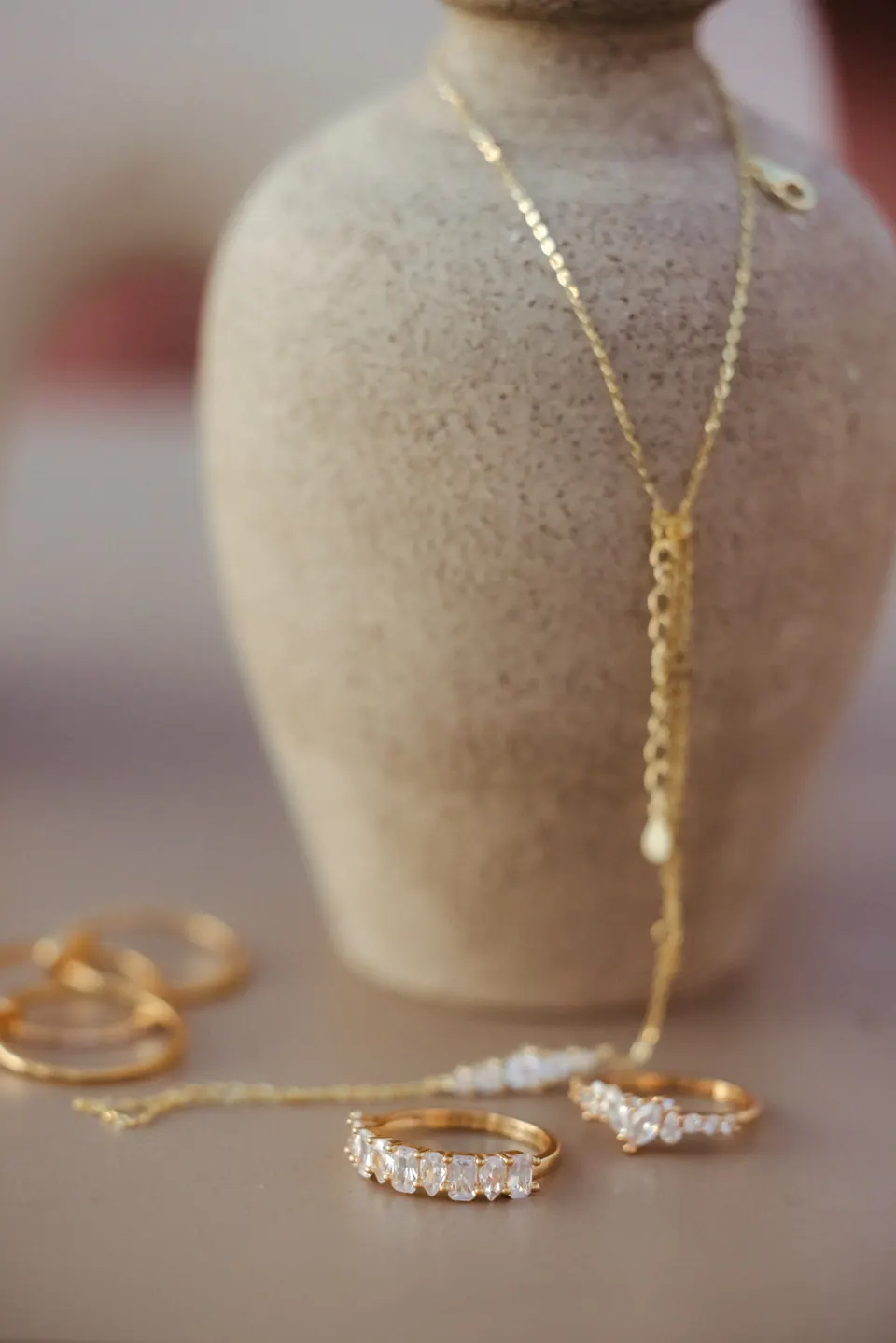 A hand chain draped over a stone-textured vase, with rings resting on the table beside it.