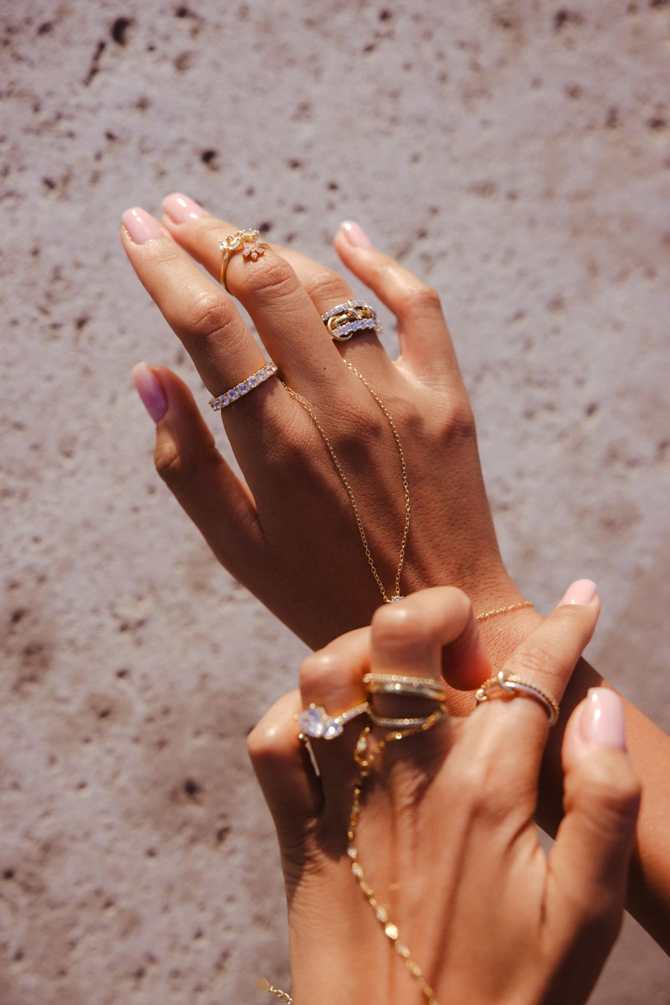 Two hands on pale stone, one wearing the Amal hand chain with rings.