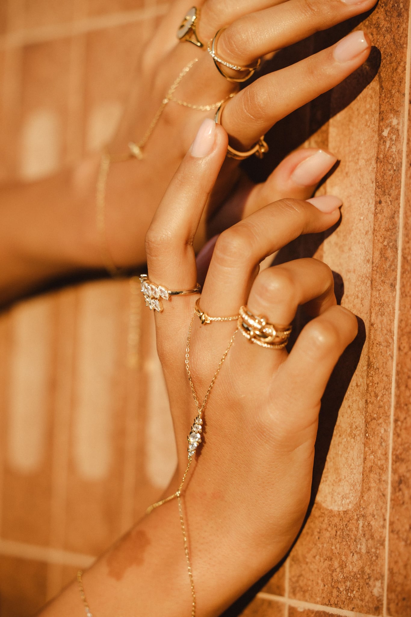 Two hands in warm golden light wearing the Amira hand chain and rings.