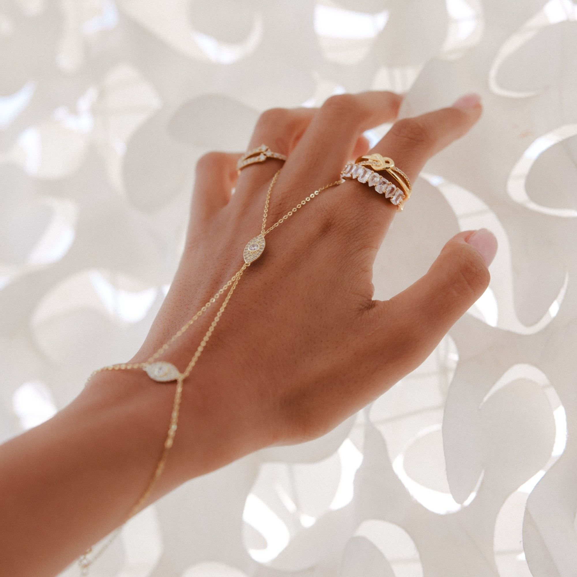 A hand wearing the Dahlia hand chain and rings among white paper petals.