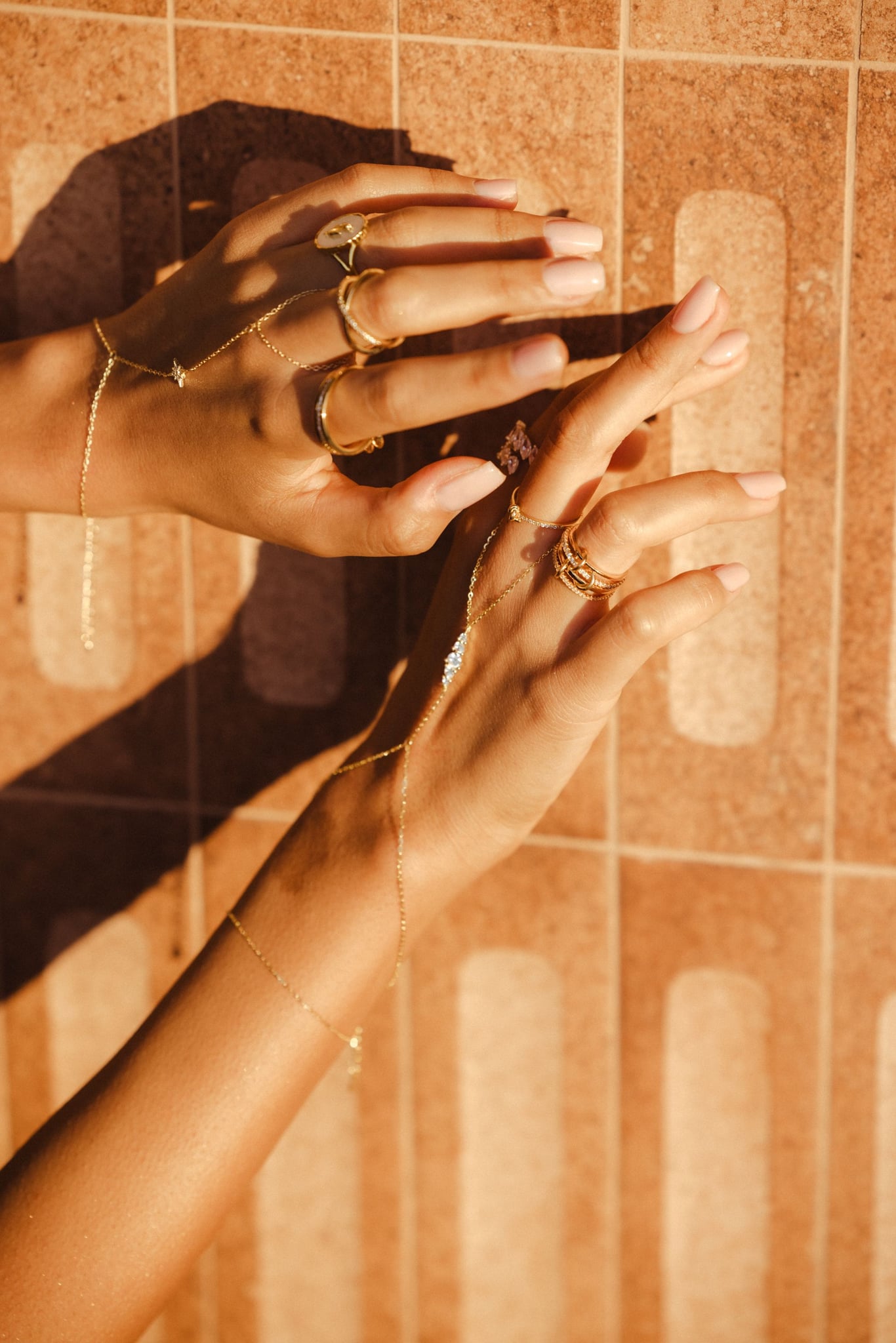 Hands in low sun against terracotta tiles, wearing the Nour hand chain and rings.