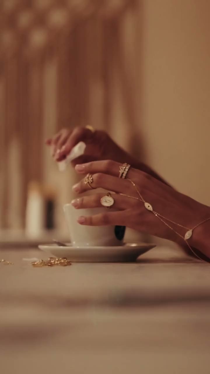 Short film: hands around a white coffee cup, wearing rings, including the Zahra ring, and a hand chain.