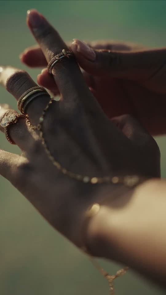 Short film: a hand with rings and a fine hand chain moving over clear, sunlit water.