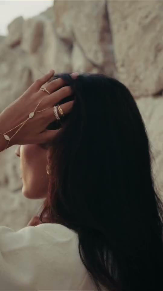 Short film: a hand in the hair against a stone wall, then hands on a white knit wearing the Dahlia hand chain.